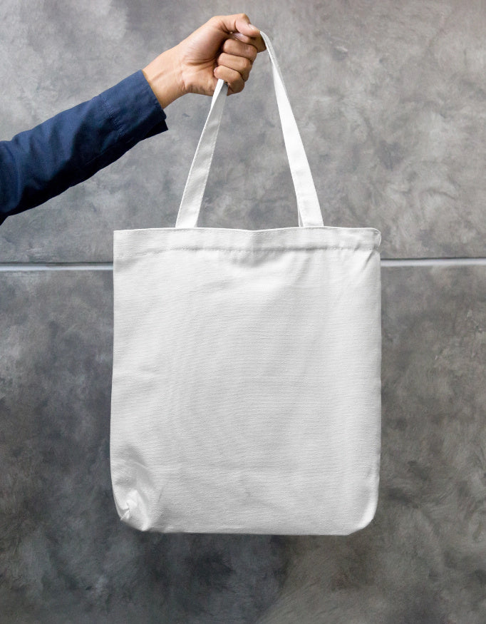 In an urban setting, a person in a beige shirt and cap carries the "Pink Petal Tote" by A Heartee Affair—an eco-friendly canvas bag with a vibrant pink and green floral design.