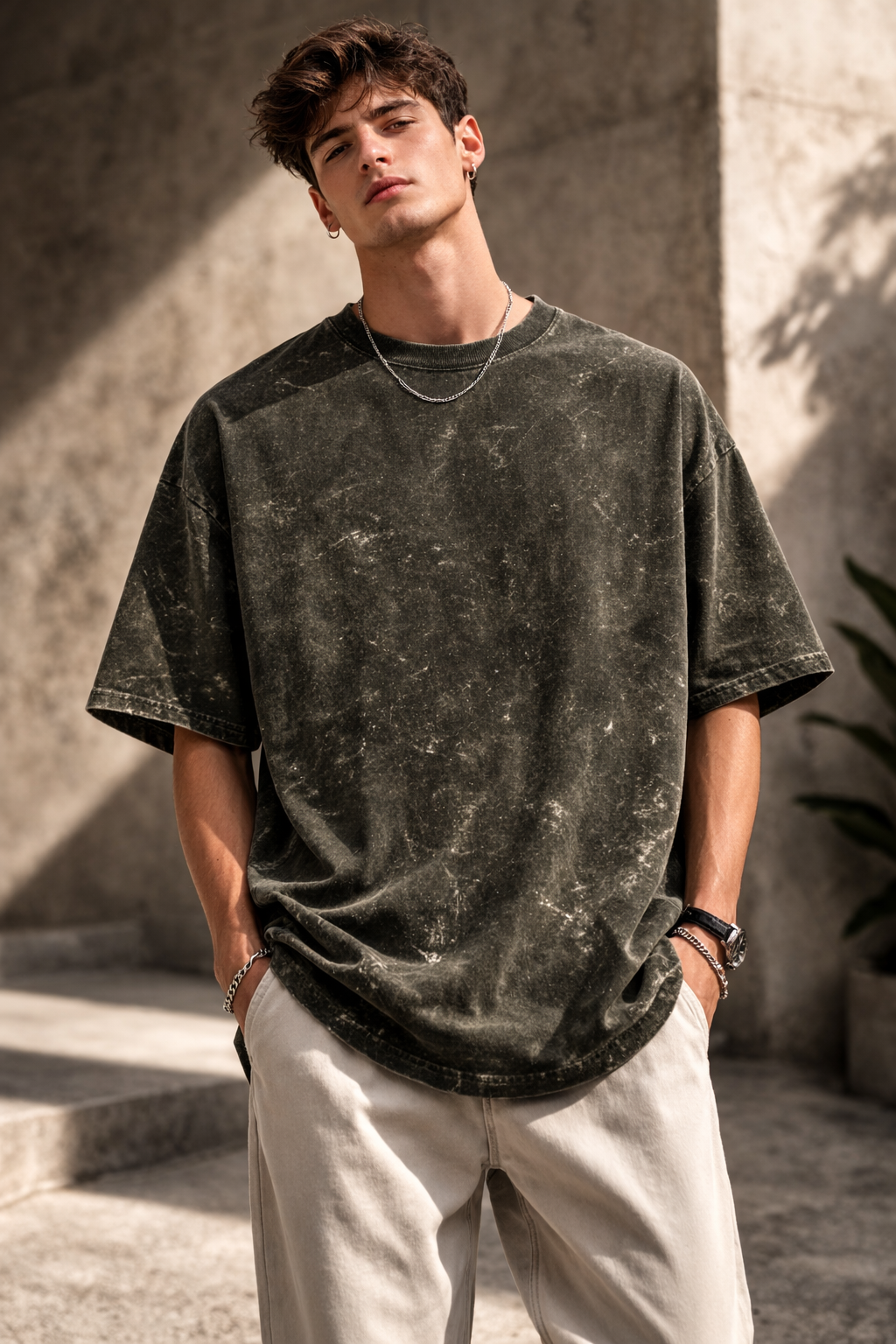A young man stands outdoors with his hands in his pockets, wearing the A Heartee Affair Unisex Acid Washed Oversized Tee and light pants, looking confidently at the camera against a concrete background in natural sunlight.