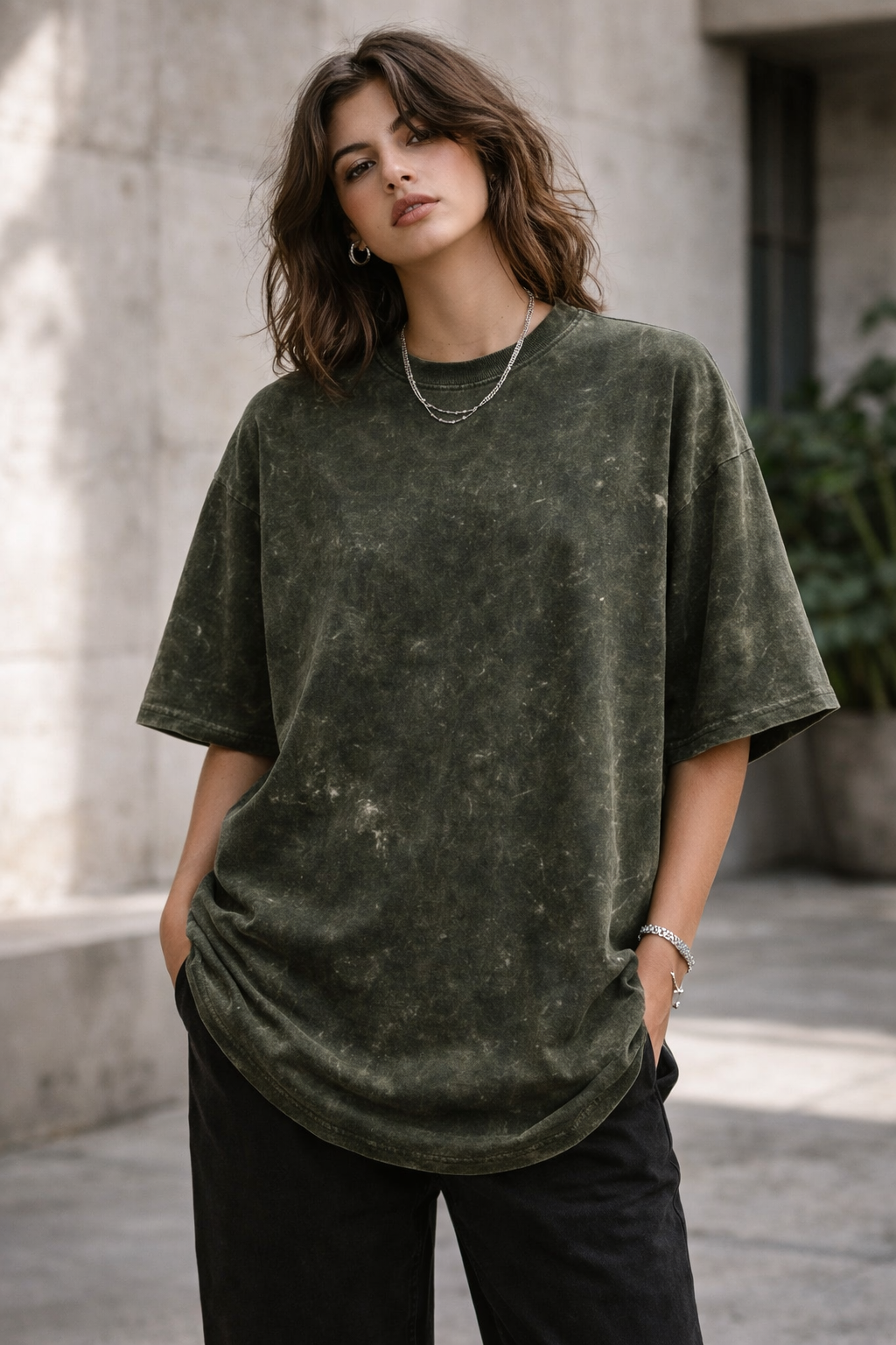 A young man stands outdoors with his hands in his pockets, wearing the A Heartee Affair Unisex Acid Washed Oversized Tee and light pants, looking confidently at the camera against a concrete background in natural sunlight.