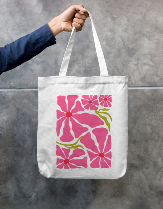 In an urban setting, a person in a beige shirt and cap carries the "Pink Petal Tote" by A Heartee Affair—an eco-friendly canvas bag with a vibrant pink and green floral design.