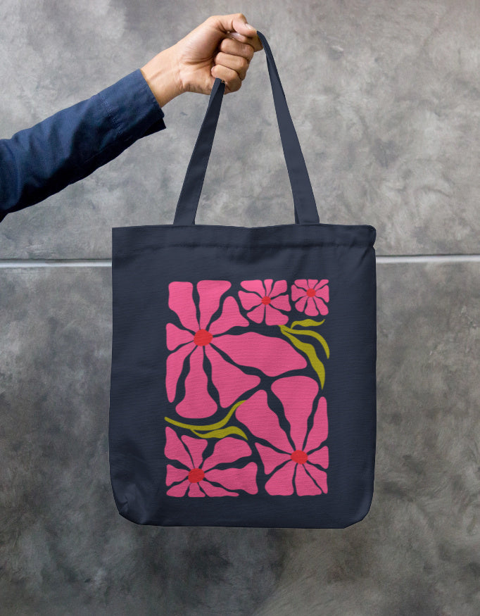 In an urban setting, a person in a beige shirt and cap carries the "Pink Petal Tote" by A Heartee Affair—an eco-friendly canvas bag with a vibrant pink and green floral design.