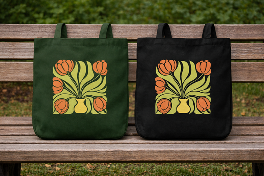 A woman in a beige shirt and green pants carries the Tulip Muse Tote by A Heartee Affair—a black cotton canvas bag with an orange tulip and green leaf design—while outdoors in an urban setting.